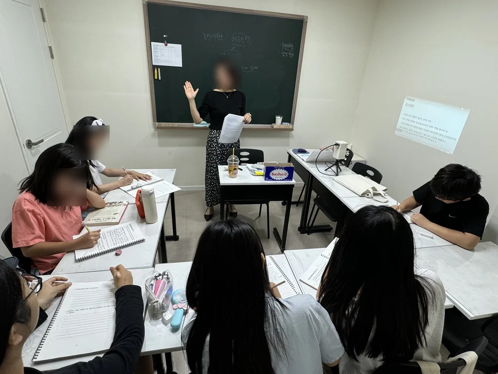 미래를 읽는 부모 학원의 단체 토론·발표 수업 — 선생님이 칠판 앞에서 주제를 이끌고 학생들이 각자 노트에 정리하고 있다